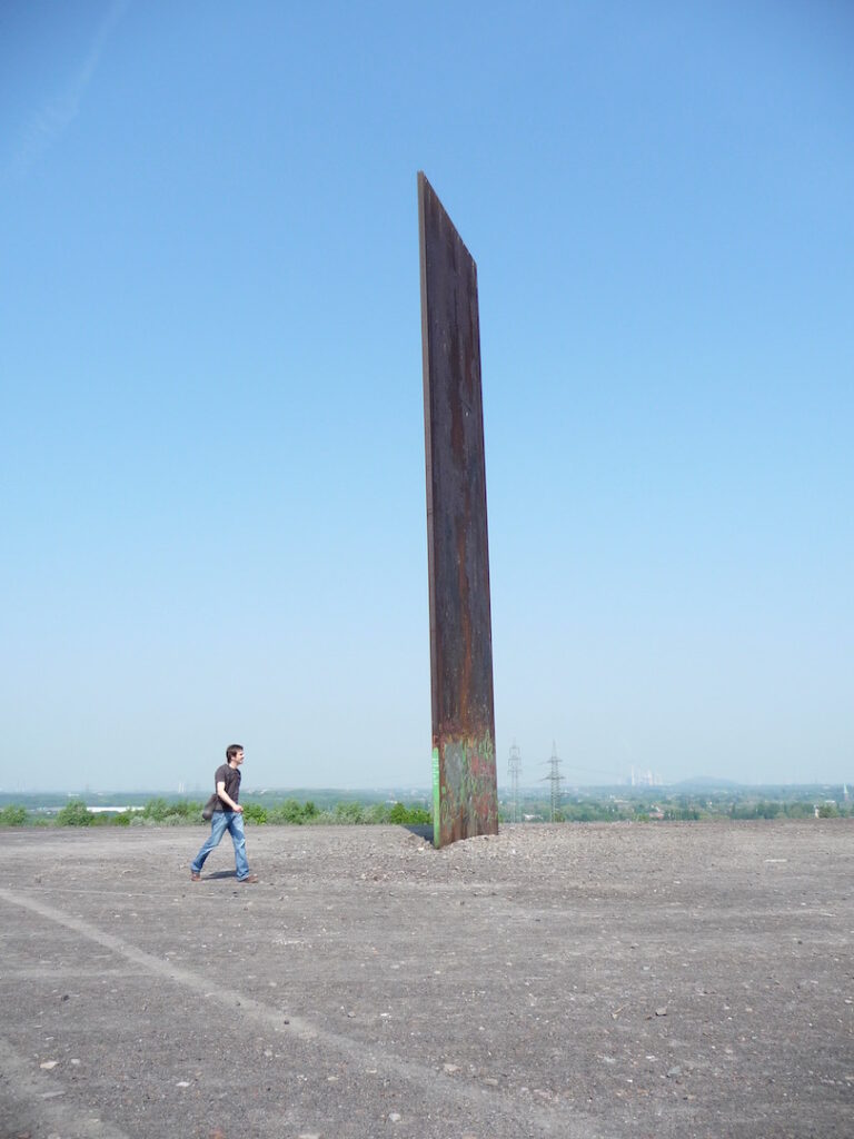 Der Mensch wirkt klein gegen die hoch ragenden Stahlbramme des Künstlers Richard Serra auf der Schurenbachhalde in Essen.

